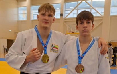 Du dziudistai baltais kimono su aukso ir bronzos medaliais sporto salėje.