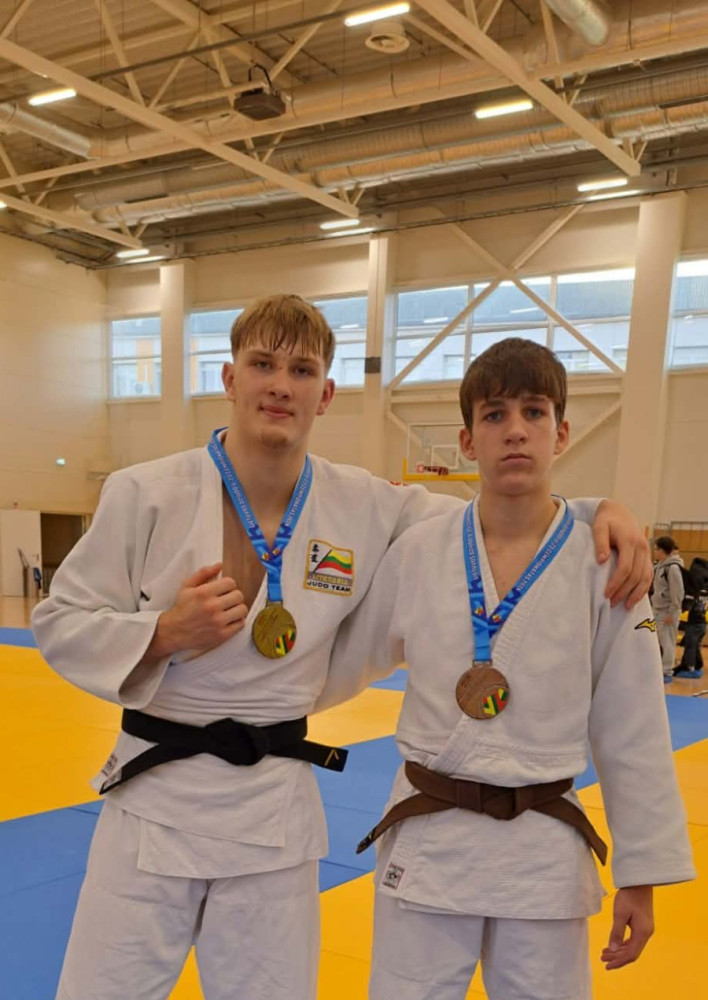 Du dziudistai baltais kimono su aukso ir bronzos medaliais sporto salėje.
