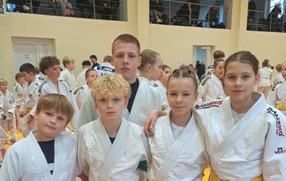 Penki jaunieji dziudistai baltais kimono sporto salėje per varžybas.