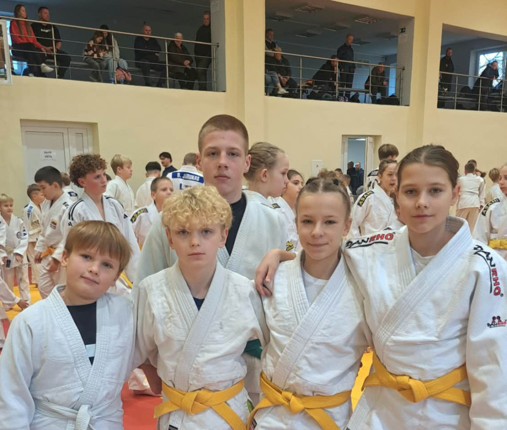 Penki jaunieji dziudistai baltais kimono sporto salėje per varžybas.
