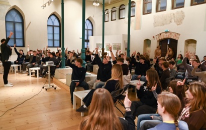 Moksleiviai pakeltomis rankomis dalyvauja „EkoLogikos“ protmūšyje.