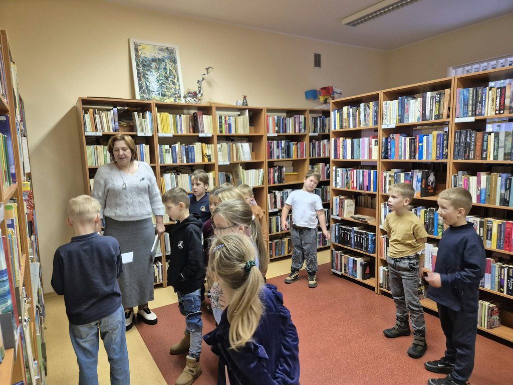 Miroslavo pirmokai su bibliotekininke tarp bibliotekos knygų lentynų.